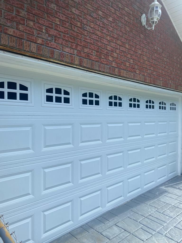 A white garage door with a brick wall behind it.