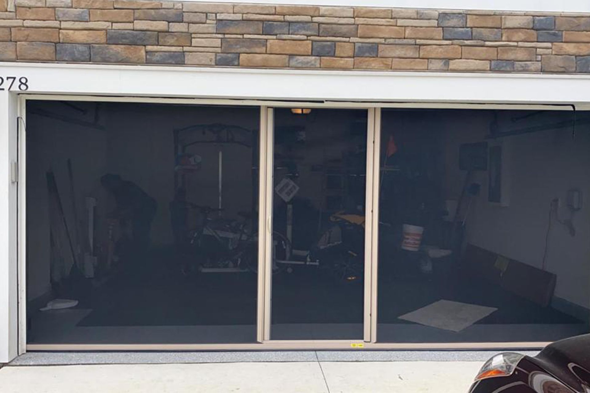 A car is parked in front of a screened in garage door.