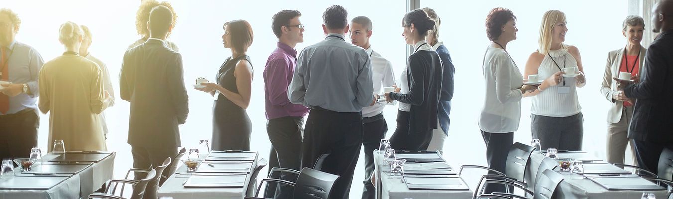 People in business attire stand around a conference table in front of a window.
