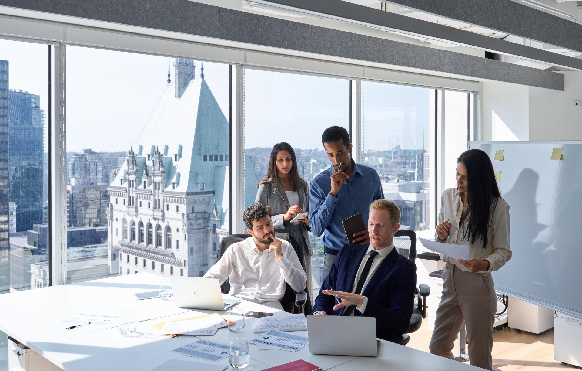 Business team in a modern office with city views, reviewing documents and brainstorming.