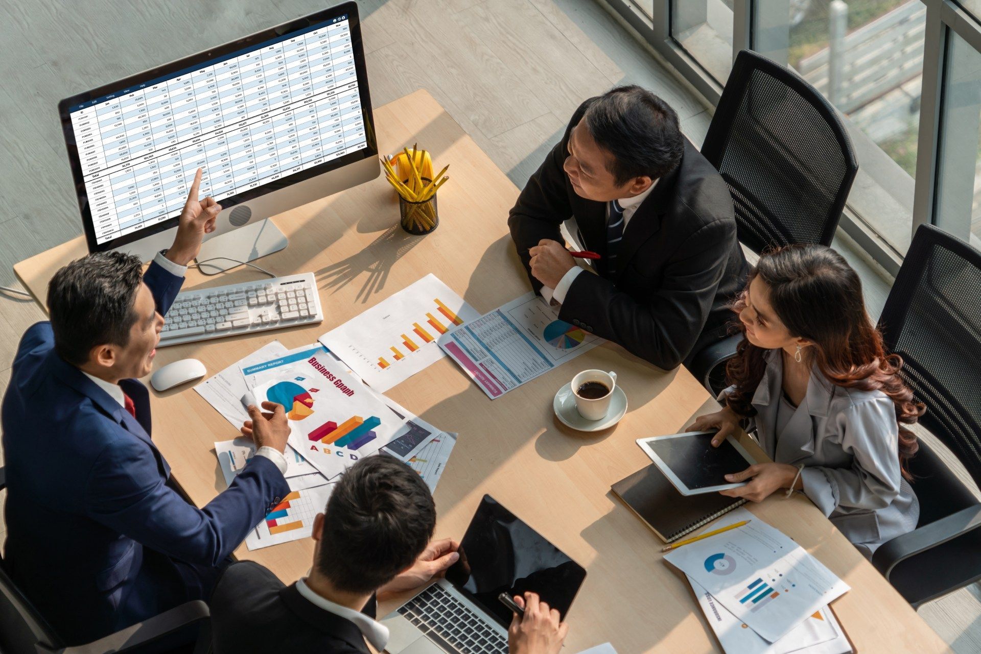 Business team in meeting, reviewing data, pointing at a computer screen and graphs.