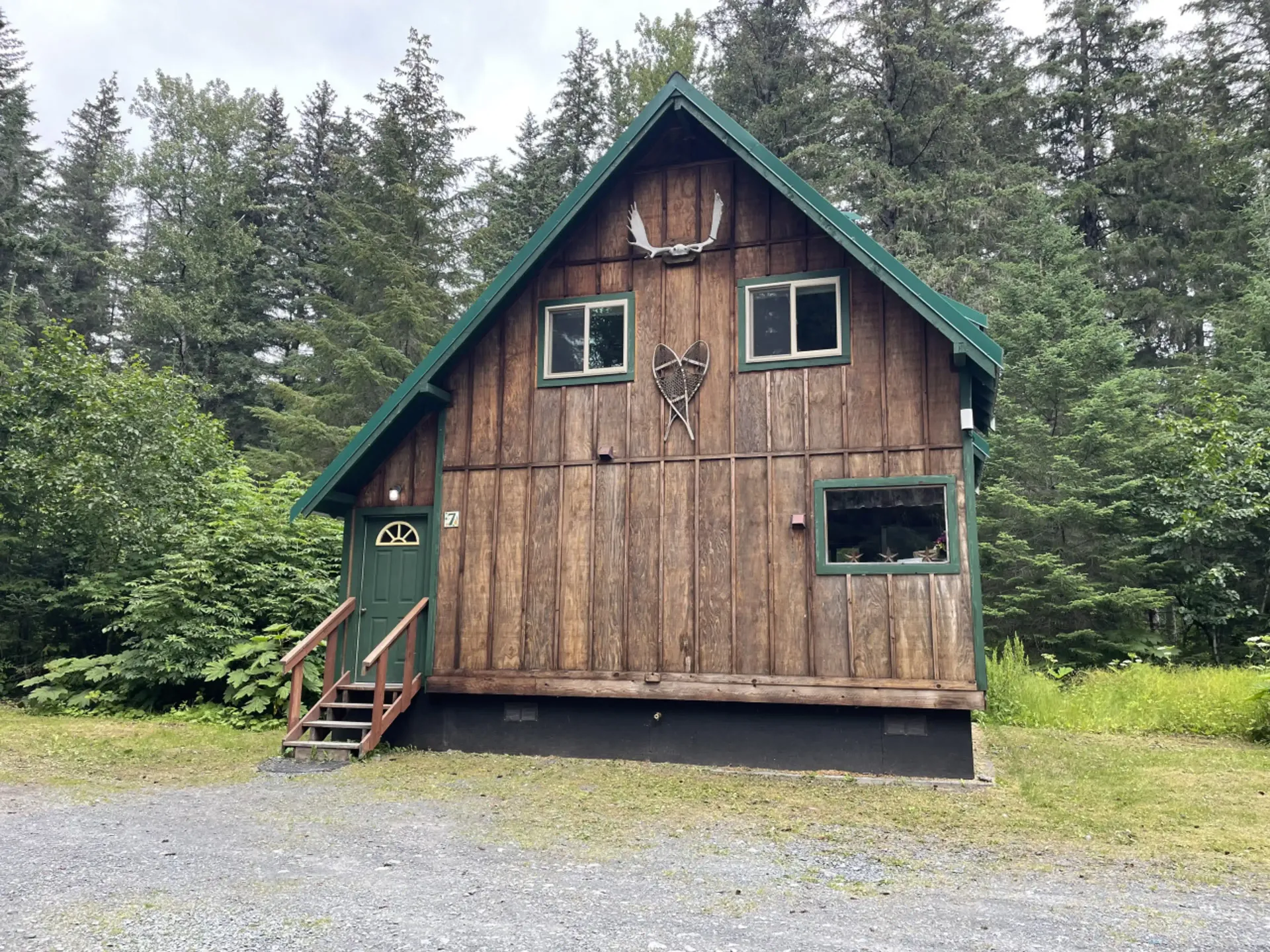 Wooden cabin in a forest with green roof and door; animal skull decoration above a window.