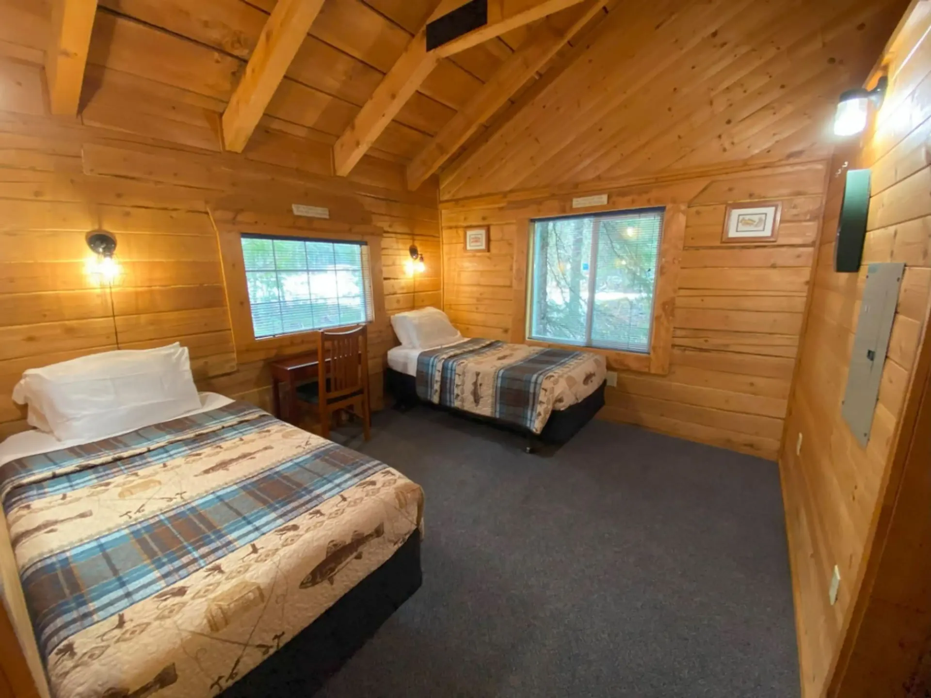 Cozy cabin interior with two twin beds, wood paneling, windows, and a desk.