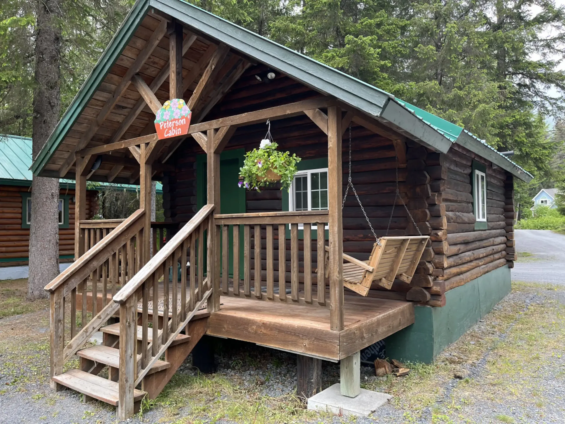 Log cabin with porch, swing, and hanging plant; green door and roof.