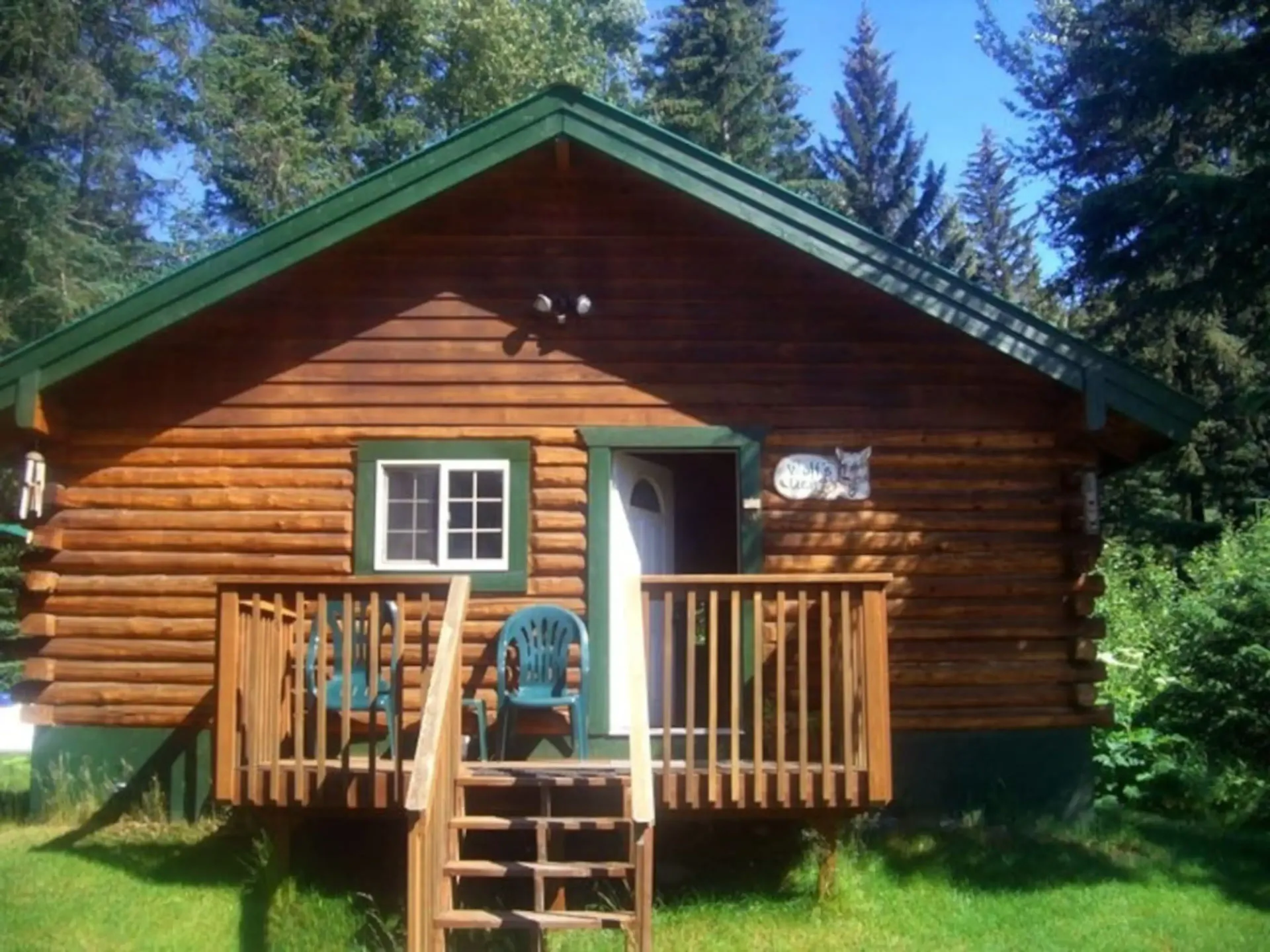 Log cabin with green trim, small porch, and steps in a grassy area.