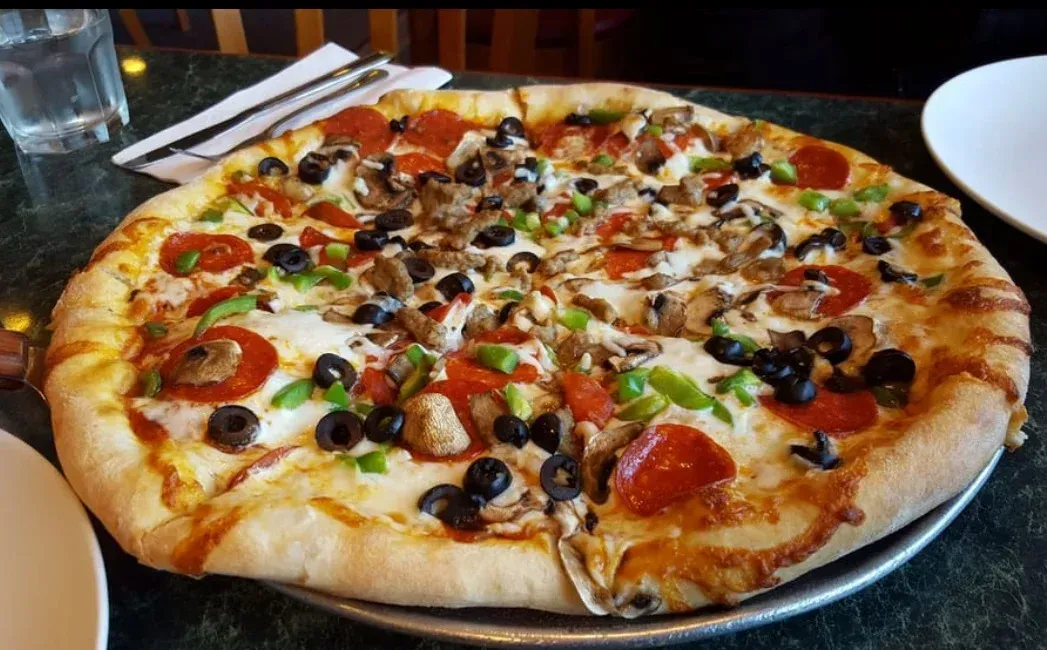 Pizza with pepperoni, black olives, green peppers, and mushrooms on a metal pan.