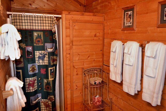 Cozy cabin bathroom with wooden walls, white towels, and a nature-themed shower curtain.