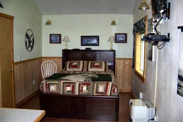 Bedroom with a bed, TV, small window, and wooden paneling. Brown furniture, light green walls.