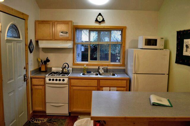 Small kitchen with light wood cabinets, a white stove, fridge, and microwave. Window over the sink.