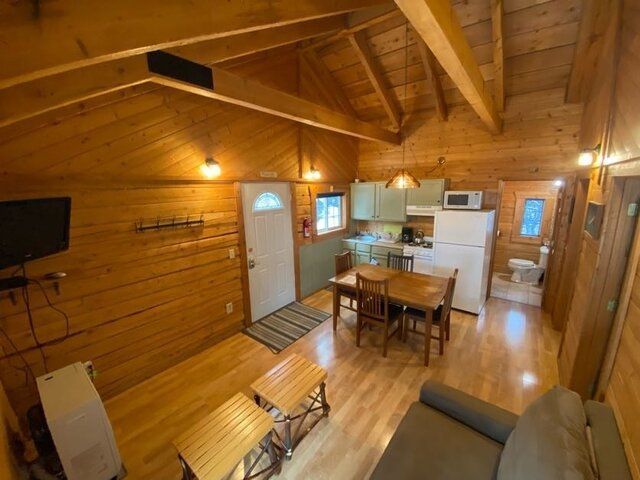 Cozy cabin interior: wood walls, small kitchen, dining area, sofa, door, and a bathroom visible.