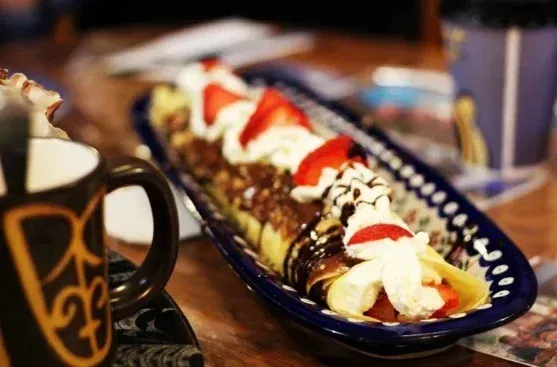 Crepe dish with strawberries, whipped cream, chocolate sauce, and coffee mug.