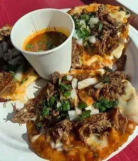 Quesabirria tacos with consommé, served on a white plate. Beef, cheese, cilantro, onion.