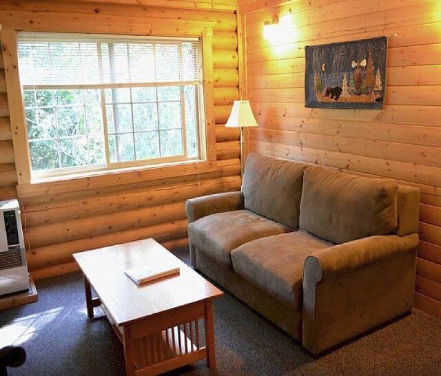 Cozy cabin living room with a tan couch, wooden coffee table, window, and art.