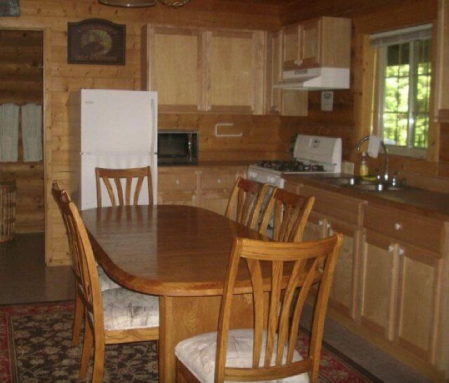 Wooden dining table and chairs in a log cabin kitchen with appliances and a window.