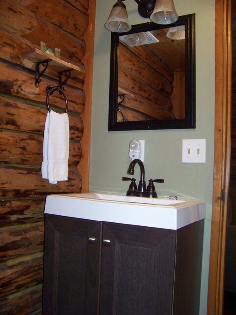 Bathroom with brown vanity, sink, mirror, towel rack, and log walls.