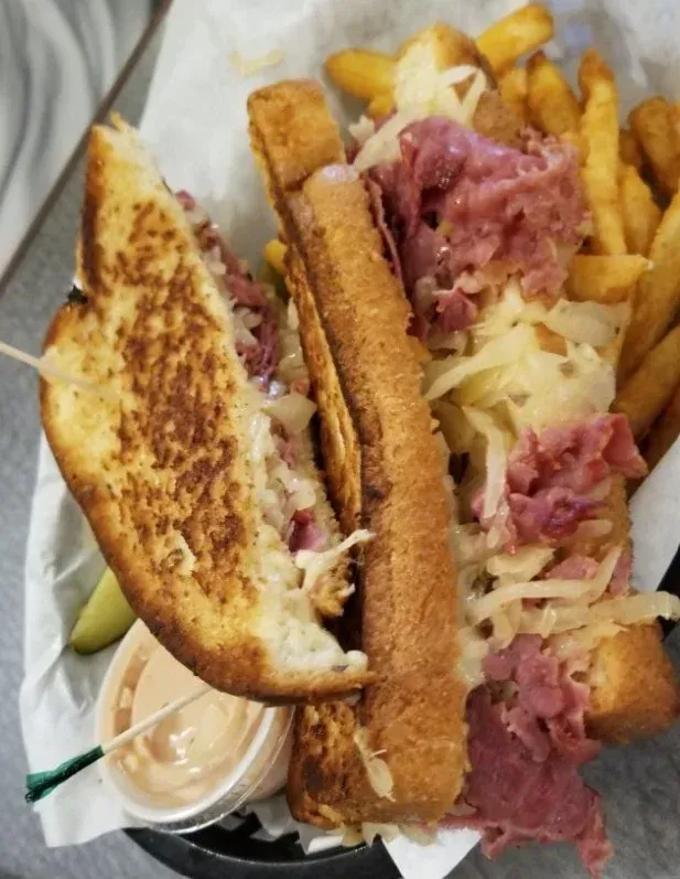 Reuben sandwich with fries and dipping sauce in a basket. Grilled bread, corned beef, sauerkraut, and Swiss cheese.