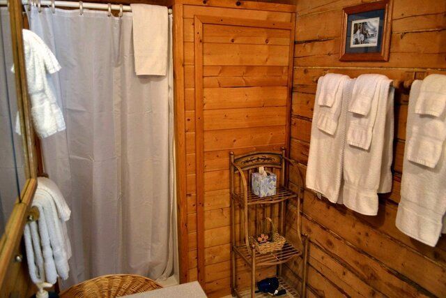 Cozy bathroom with wood paneling. White towels, bathrobes, and shower curtain. Small metal shelf.