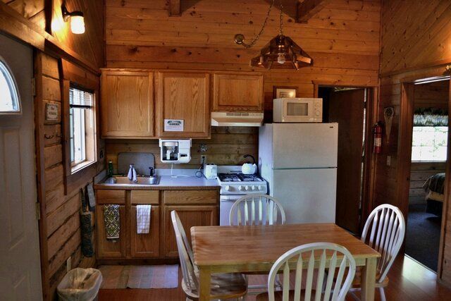 Small cabin kitchen with wooden walls, featuring a table, stove, refrigerator, and cabinets.
