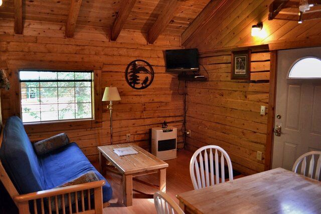 Cozy log cabin interior with blue futon, small table, TV, dining table, and chairs.