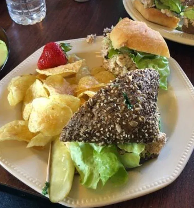 Plate with two sandwiches, chips, strawberry, and pickle.