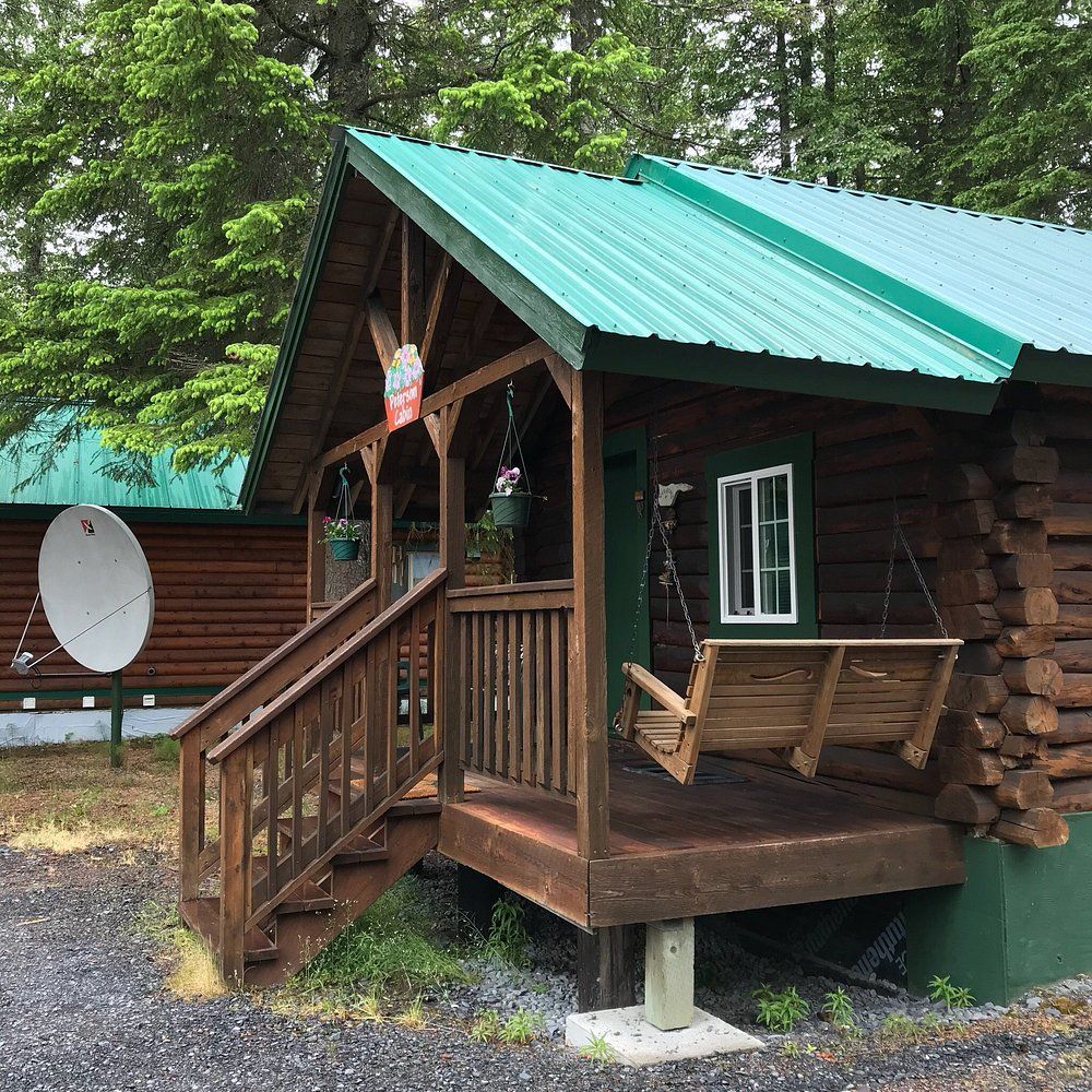 Log cabin with green roof, front porch, porch swing, and satellite dish.