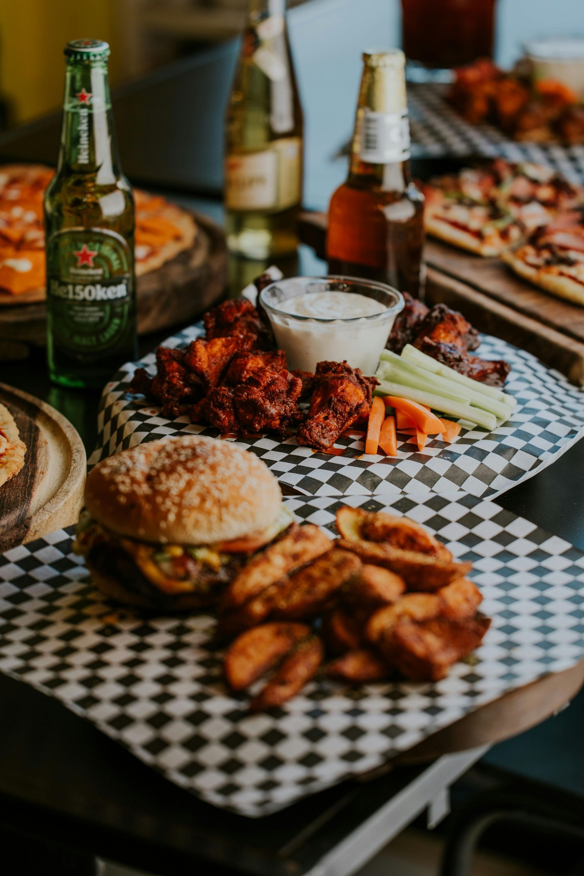 A table with burgers, chicken wings, onion rings, and beer bottles.