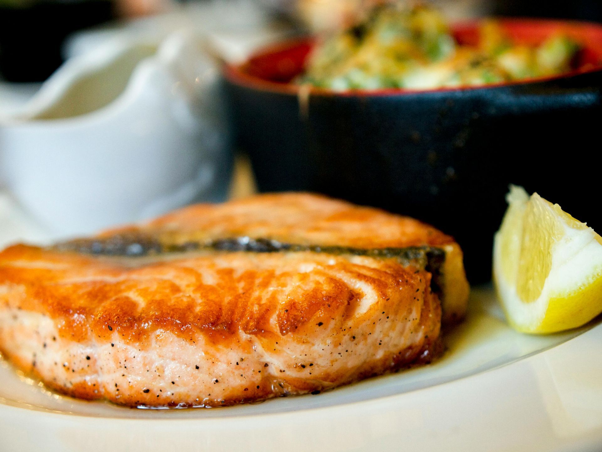 Seared salmon fillets on a plate with a lemon wedge, sauce, and a side dish.