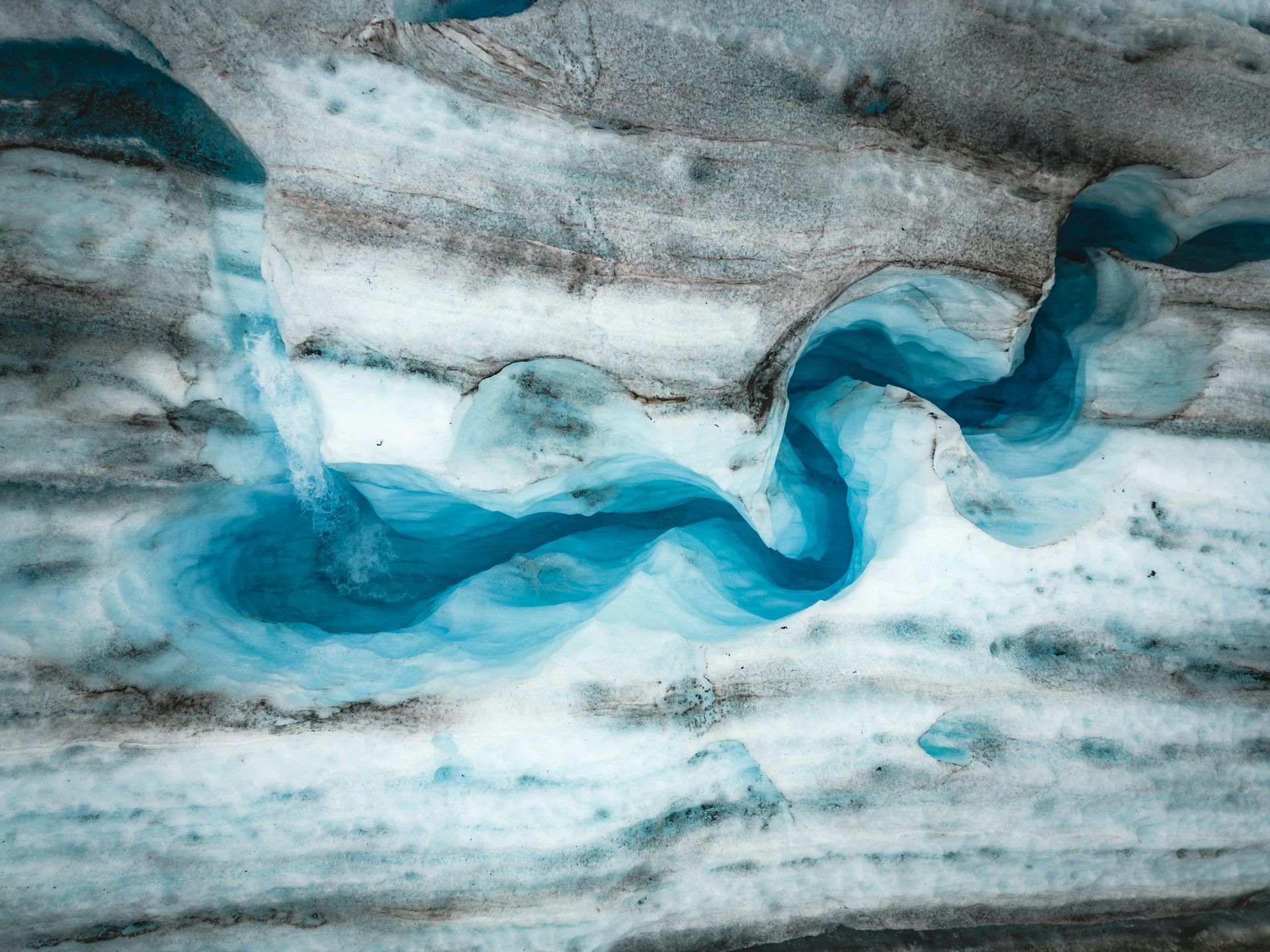 Swirling turquoise meltwater on a glacier's icy, gray surface.