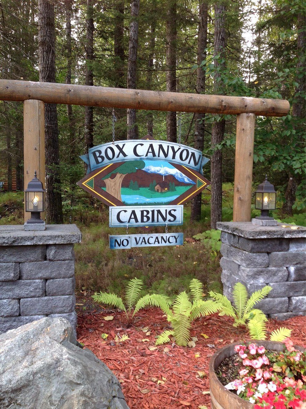 Sign for Box Canyon Cabins; brown archway, stone pillars, surrounded by trees,