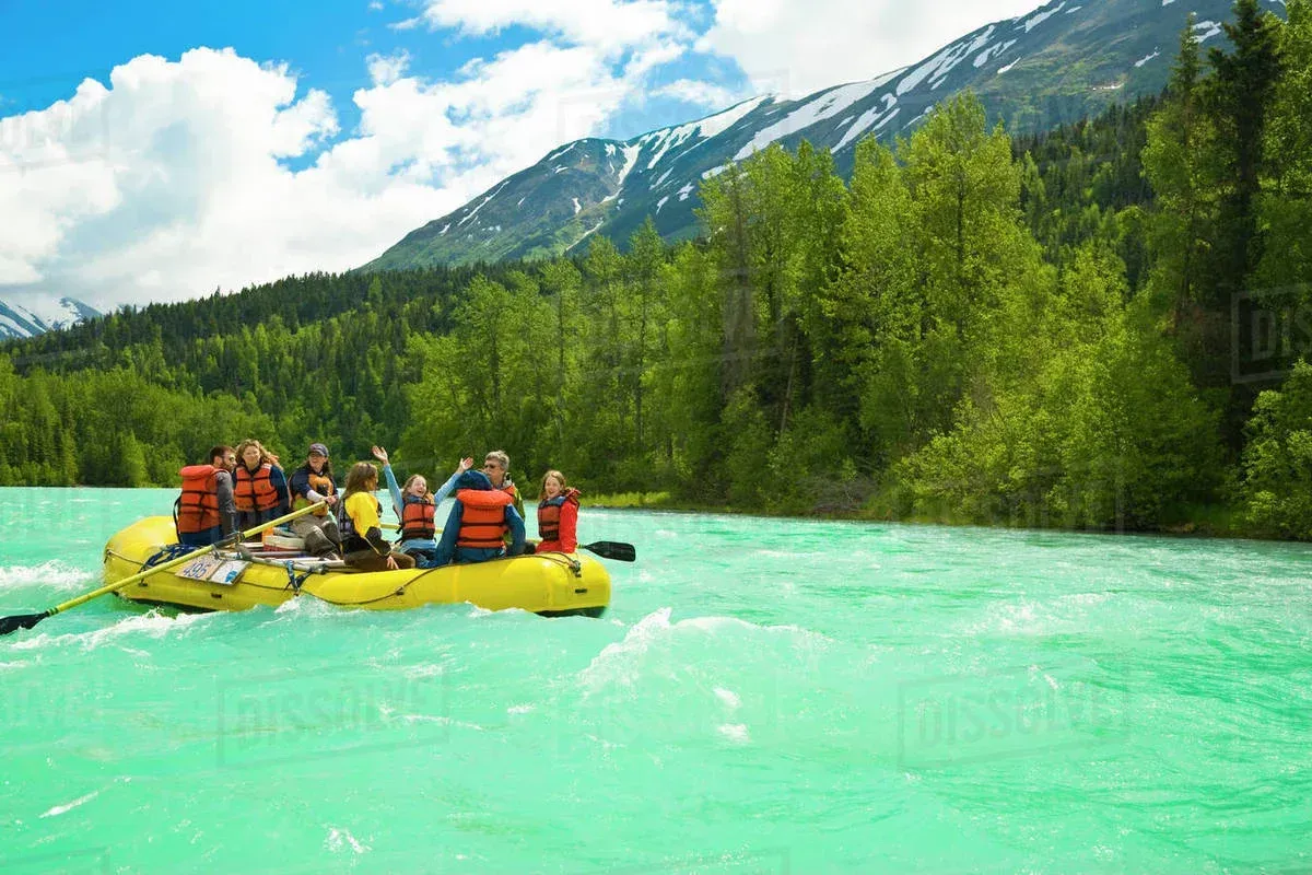 People rafting on a bright turquoise river near mountains and lush green trees.