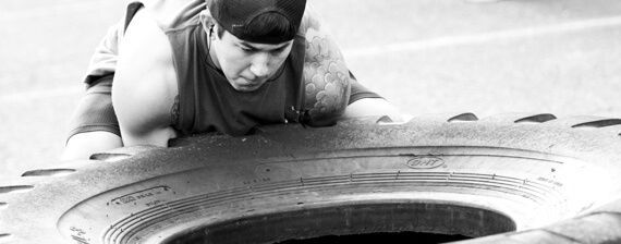 A man is crawling on top of a tire in a black and white photo.