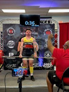 A man is squatting on a barbell in a lifting competition.