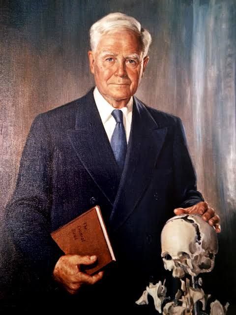 A man in a suit and tie is holding a book and a skull
