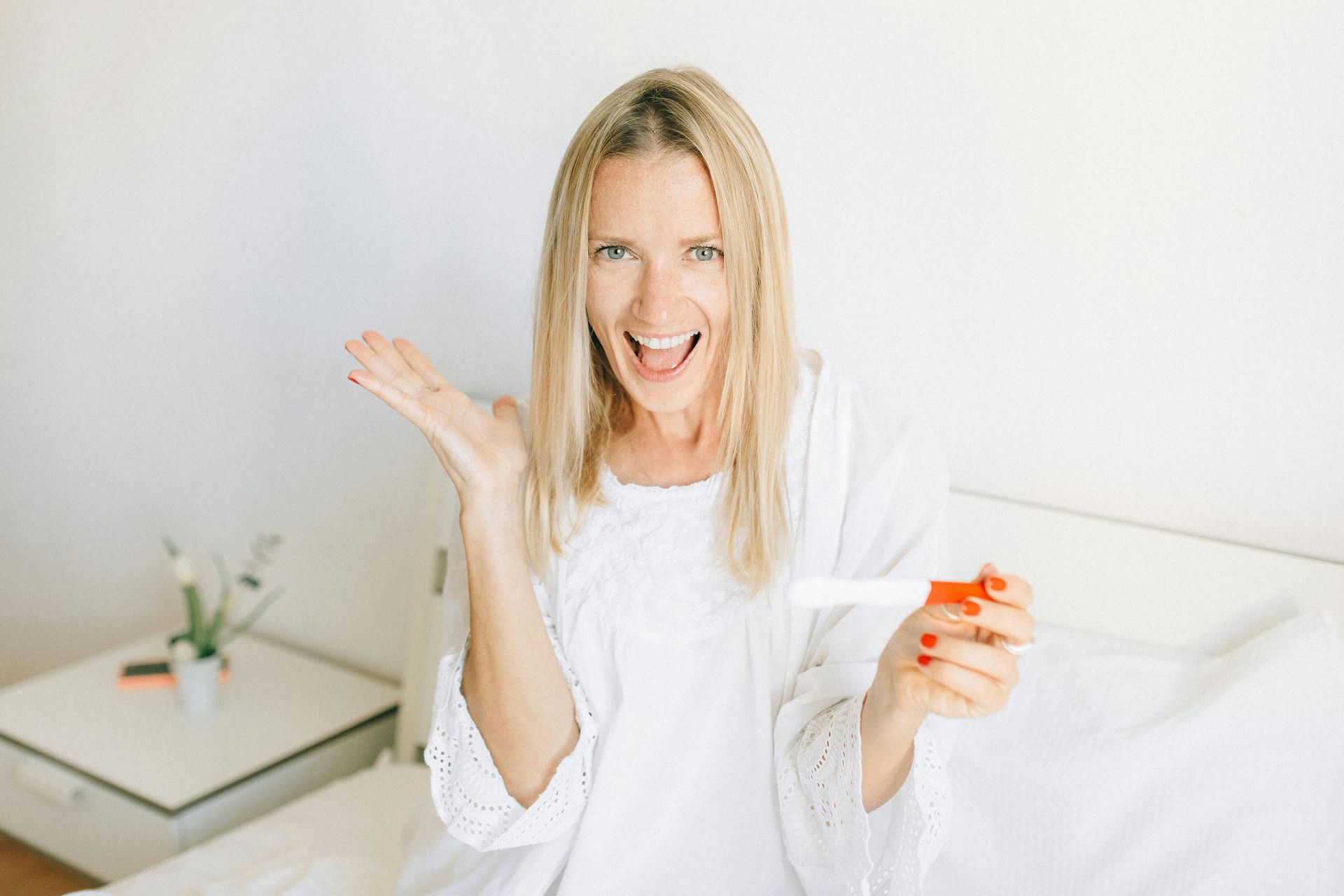 A woman is sitting on a bed holding a pregnancy test.