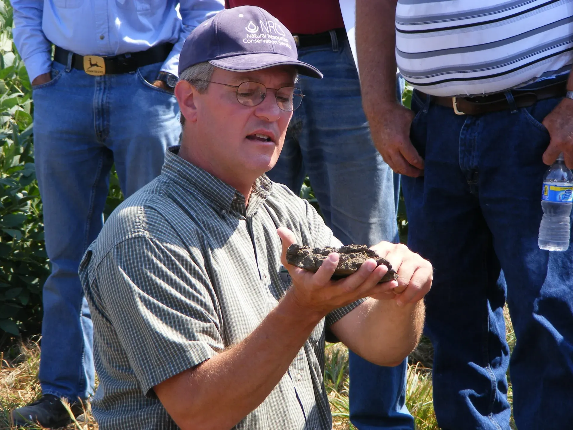Man holding soil, surrounded by people, outdoors.