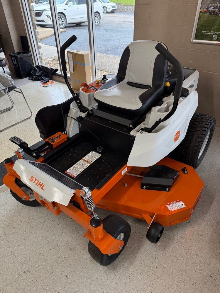 White and orange STIHL zero-turn lawn mower on display indoors, near a window.