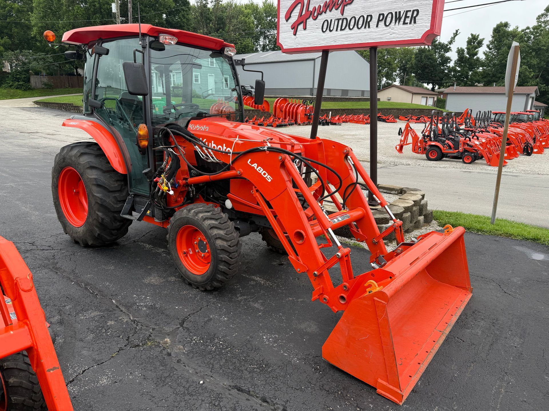 Orange tractor with front loader and backhoe parked in front of a building with a "Dixie Chopper" sign.