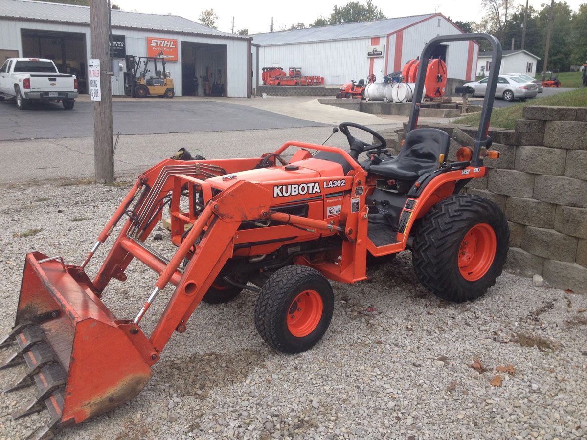 Orange Kubota tractor with a front-end loader parked on gravel in front of a building.