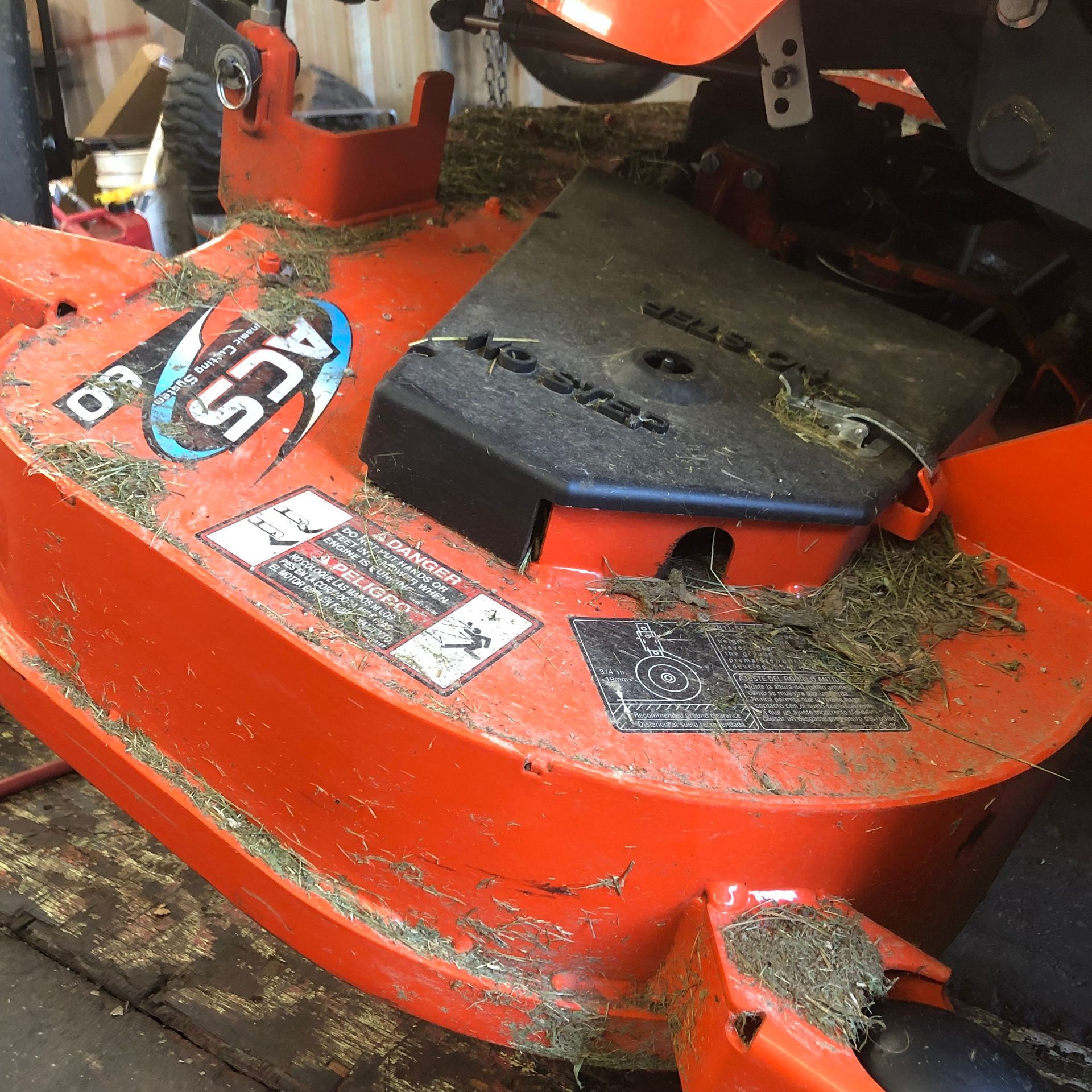 Orange lawnmower deck covered in grass clippings. Black cover is on top.