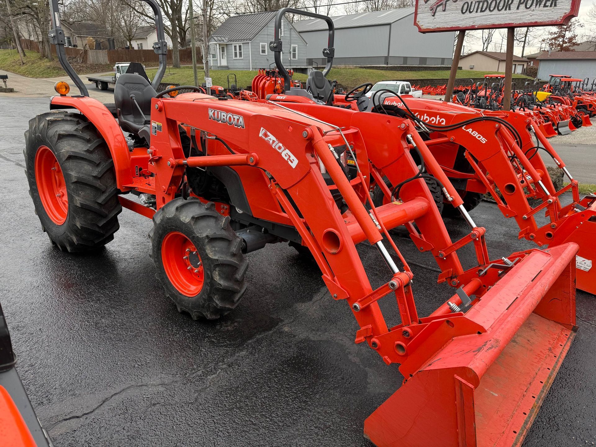 Orange tractor with front loader parked outside, overcast day.