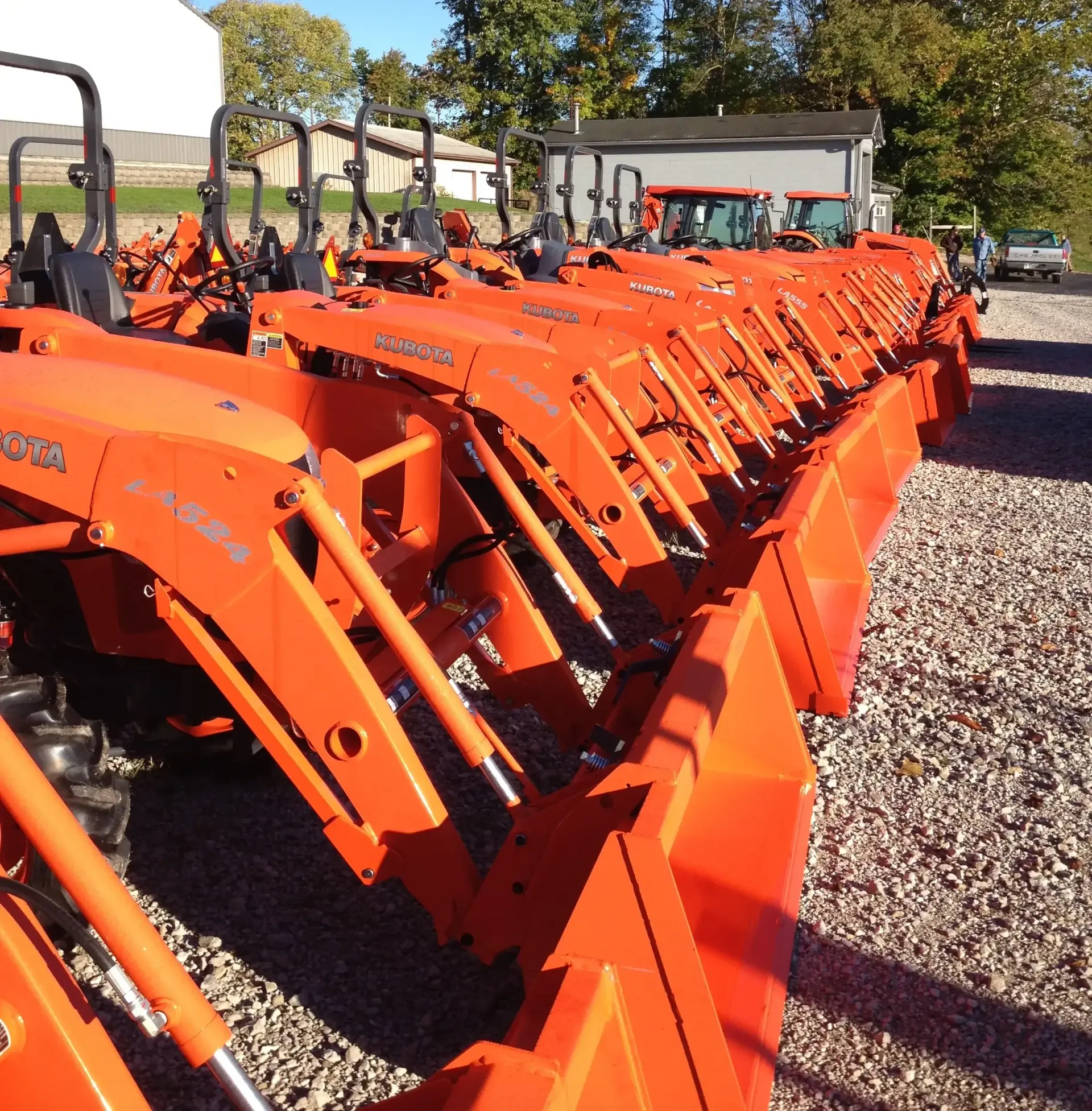 Row of new orange tractors parked outside a building on a sunny day.