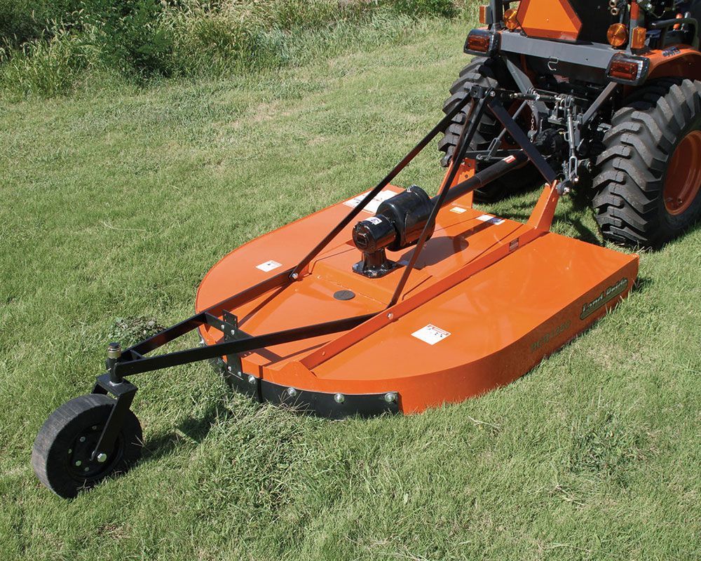 Orange rotary mower attached to a tractor, cutting grass in a field.