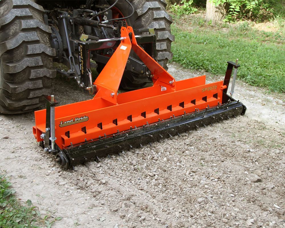 Orange road drag with spikes attached to tractor, leveling gravel driveway.