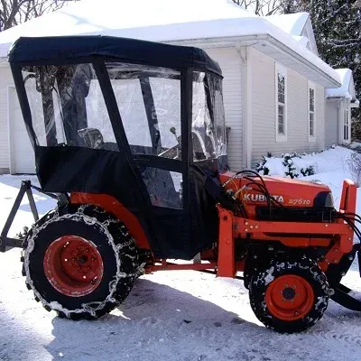 Orange Kubota tractor with a black cab and snow chains, plowing snow in front of a house.