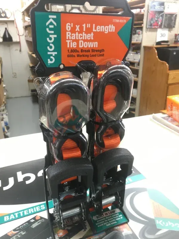 Display of Kubota ratchet tie-downs, with black and orange straps, in a store setting.