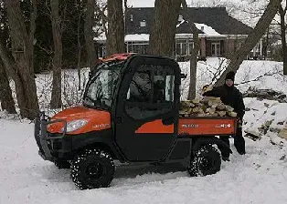 Orange Kubota utility vehicle with a person loading firewood in the snow.