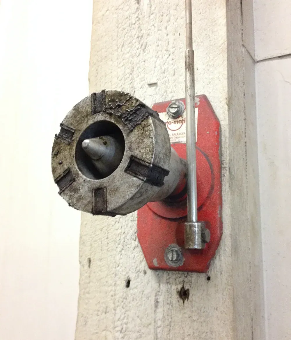 Red fire hose connection on a concrete pillar. Gray metal nozzle with black rubber and a metal rod handle.