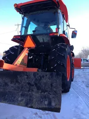 Orange tractor with a snow blade, clearing snow on a street.