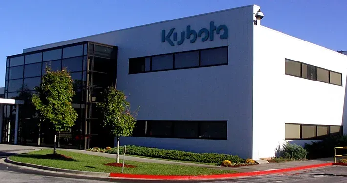 Kubota corporate building exterior, two-story white structure with blue logo, large windows, and manicured landscaping.