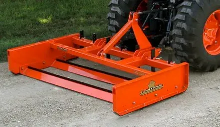Orange box blade attachment connected to a tractor for grading gravel.